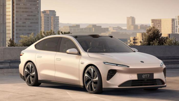 Marketing image of the Nio ET7 EV. The goldish-beige car sits on a lot overlooking a city skyline during daytime.