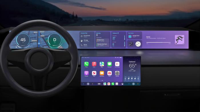 Interior shot of a car's steering wheel and dash. Apple CarPlay featured on the main screen and elongated dash screen. Nighttime with a dim silhouetted view ahead.