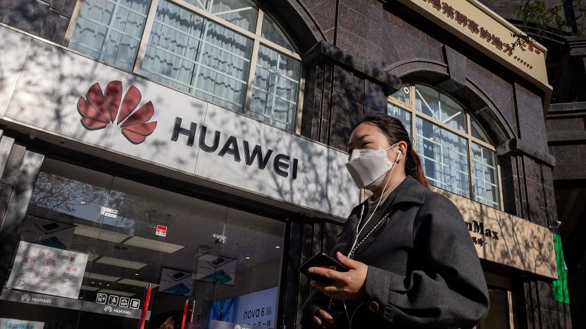 A woman wearing a face mask amid concerns over the COVID-19 coronavirus walks holding her smartphone past a Huawei shop (L) on a street in Beijing on April 22, 2020. - China's economy shrank for the first time in decades last quarter as the coronavirus paralysed the country, in a historic blow to the Communist Party's pledge of continued prosperity in return for unquestioned political power. (Photo by NICOLAS ASFOURI / AFP) (Photo by NICOLAS ASFOURI/AFP via Getty Images)