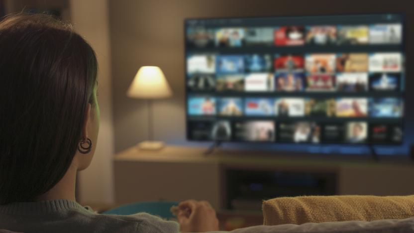 Young woman relaxing on the couch at home and watching videos on demand on her TV, entertainment concept