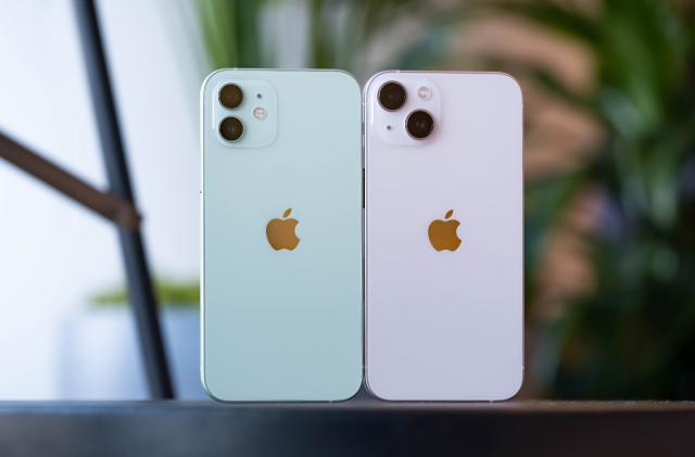 A green iPhone 12 and pink iPhone 13 with their backs facing the camera. You can see their dual cameras. On the left, the pair of sensors are stacked on top of each other. On the right, they're laid out diagonally. The module on the right is also slightly wider and taller, and the cameras themselves are slightly bigger.