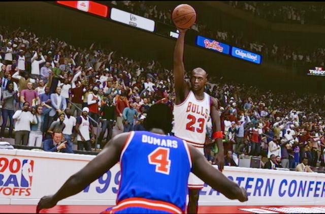 A still image from NBA 2K23 Jordan Challenge video game showing Jordan raising the ball up high in one hand as he squares off against an opposing player.