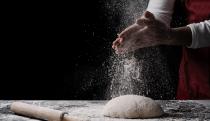 baker preparing bread dough on black table in front of yellow background