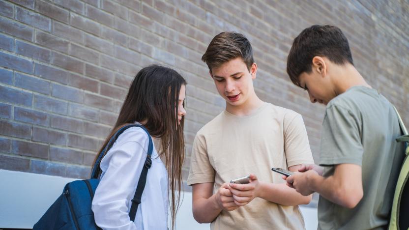 Three students, two boys and one girl checking mobile phones at school or university backyard