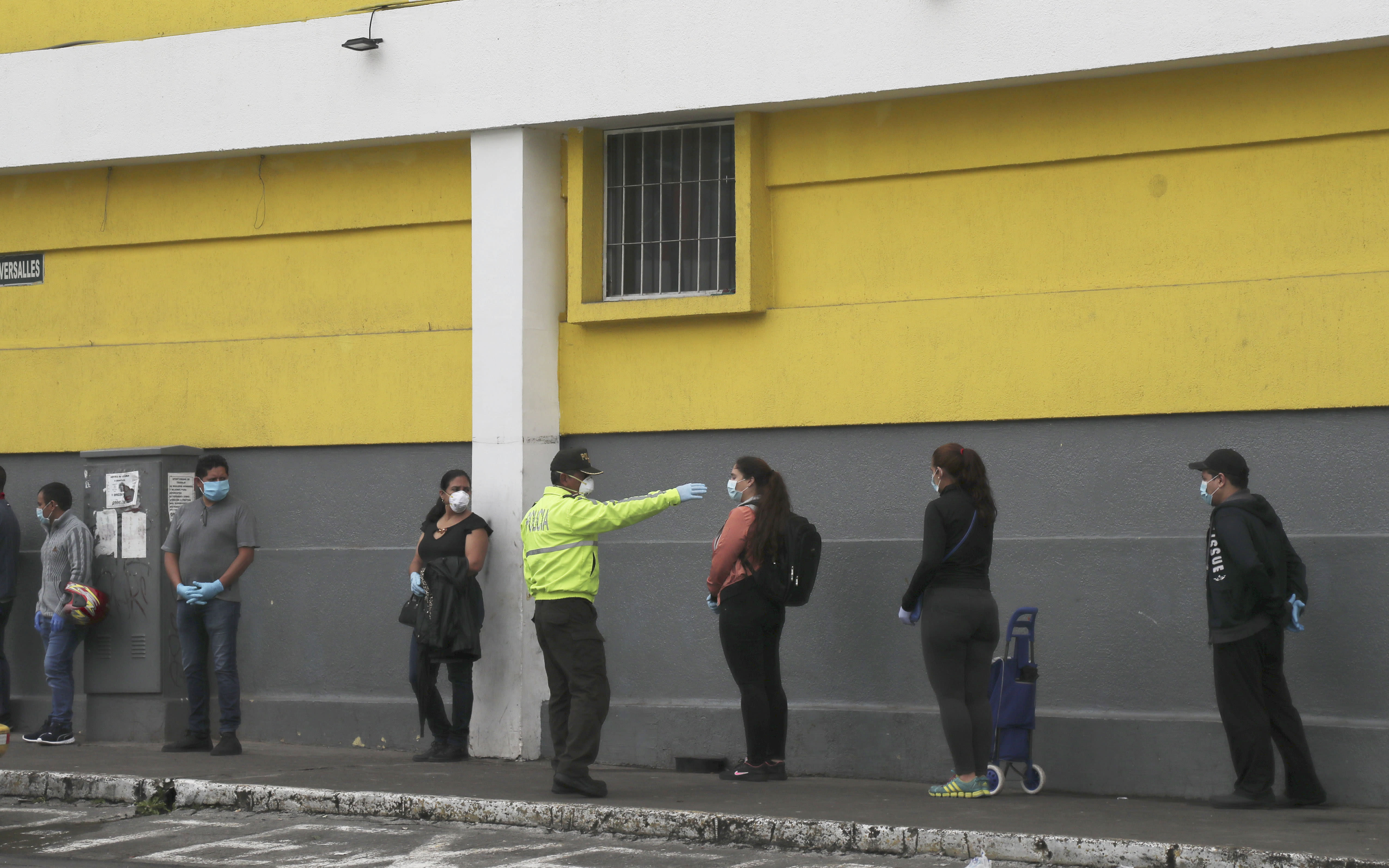 A police officer instructs shoppers to maintain a social distance as a precaution against the spread of the new coronavirus, as they wait in line to enter a supermarket in Quito, Ecuador, Saturday, March 28, 2020. The government has declared a health emergency, enacting a curfew and restricting movement to only those who provide basic services. (AP Photo/Dolores Ochoa)