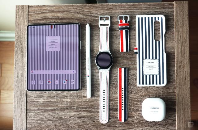 The Galaxy Z Fold 3, S Pen Pro, Galaxy Watch 4 and Buds 2 in Thom Browne editions laid out on a wooden surface.