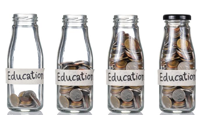 Four glass bottles sitting next to each other with growing stacks of coins inside of them. Each bottle has a piece of tape on it that says "Education."