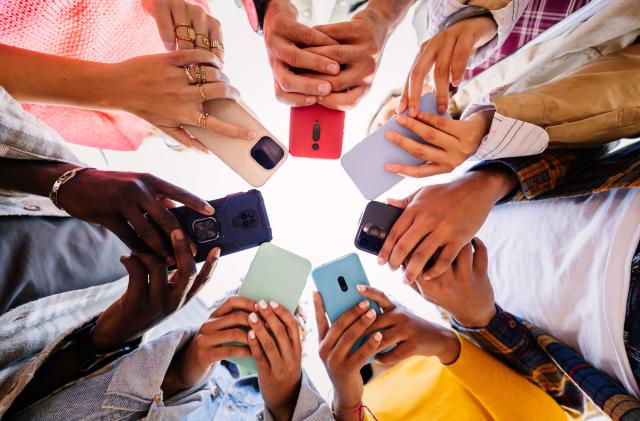 Young group of student people using smartphone together outside. Addicted millennial friends using cell phone at city street. Low angle view.