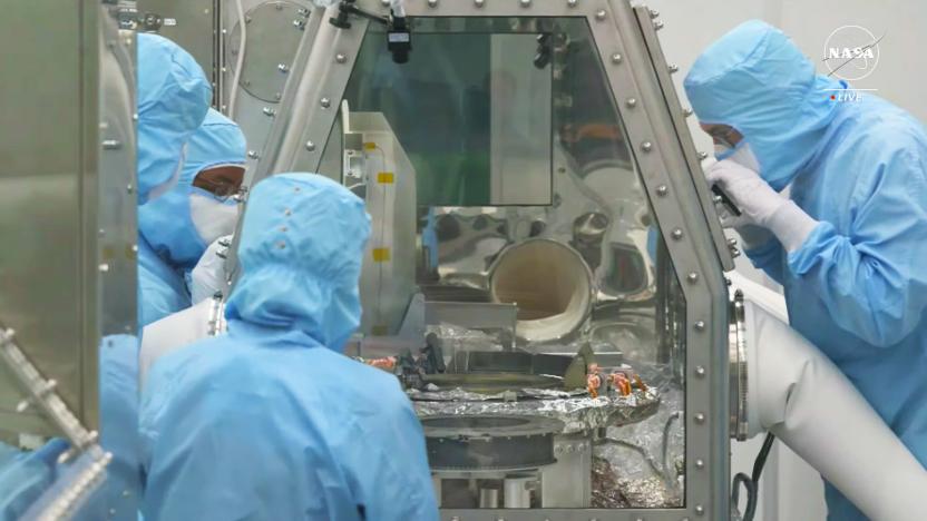 Several scientists peer into a sealed glass module where the asteroid Bennu samples stored.