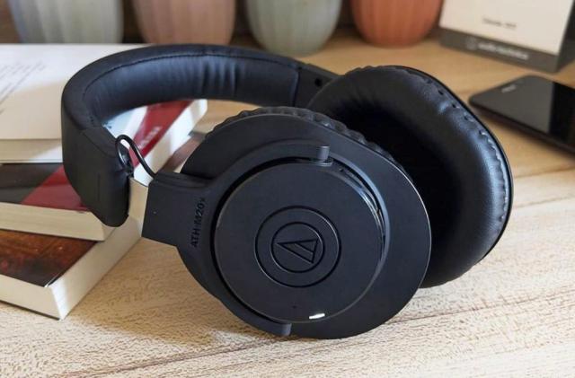 The Audio-Technica ATH-M20xBT headphones sit on a desktop amongst books, small planters and a phone.