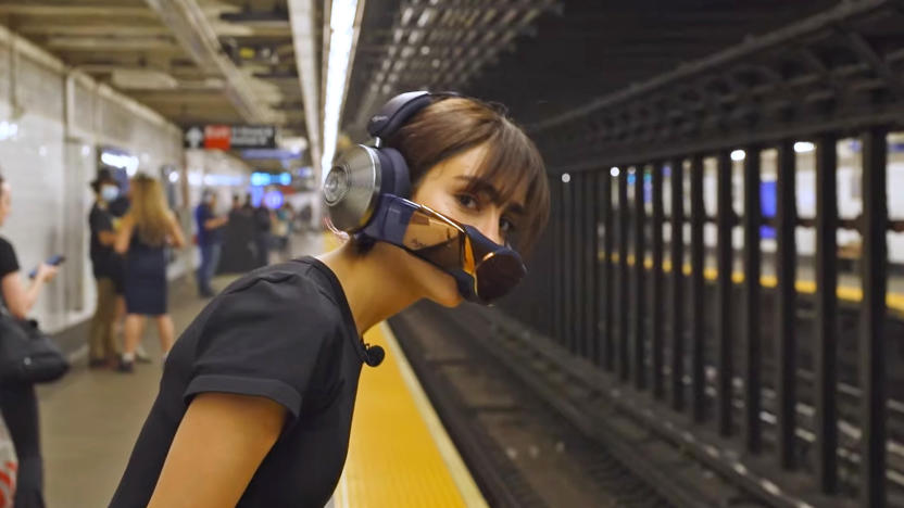 A young woman wearing the Dyson Zone headphones and breathing mask leans over the subway platform edge to see if a train is coming.