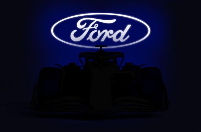 A brightly-lit Ford logo sits above a Formula 1 car shrouded in shadow.