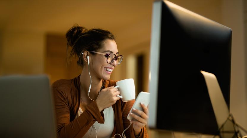 Young happy woman using cell phone while drinking tea and working at night at home.