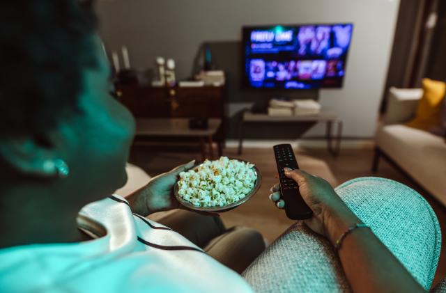 Cheerful smiling woman is watching TV and holding the remote control. Cozy night at home