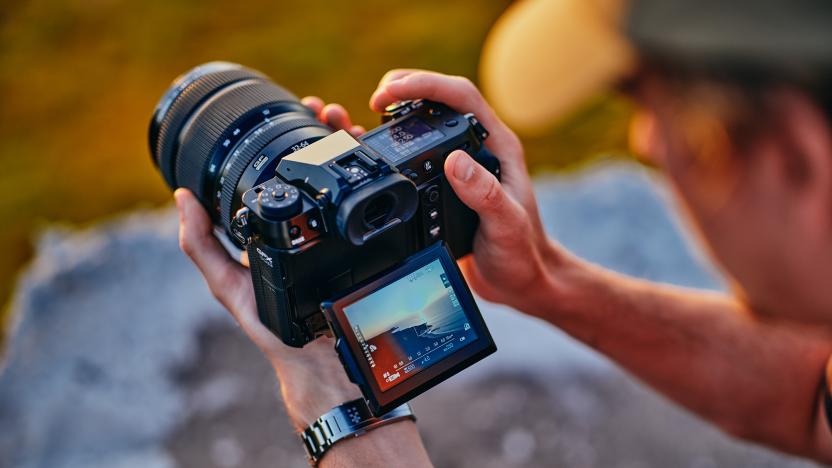 A person holding the Fujifilm GFX 100S II camera with its viewfinder folded out. View from slightly above their left shoulder.