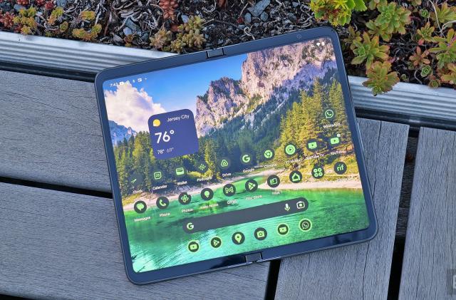 The Google Pixel Fold seen from above in its wide-open tablet-like form as it rests on a bench connected to a planter (small plants are seen in the edge of the shot).