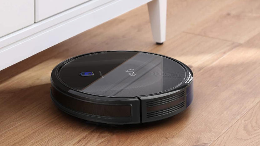 the eufy BoostIQ RoboVac 11S MAX robot vacuum is running on a hardwood floor and about to clean under a cabinet. 