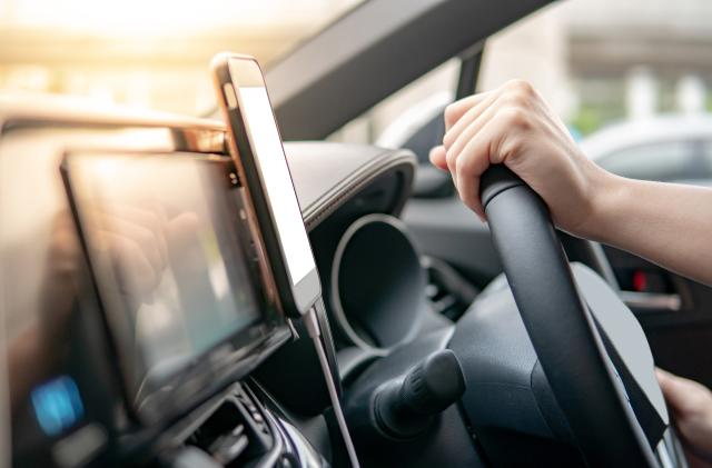 Male driver hand holding on steering wheel using smartphone for GPS navigation. Mobile phone mounting with magnet on the car console in modern car. Urban driving lifestyle with mobile app technology