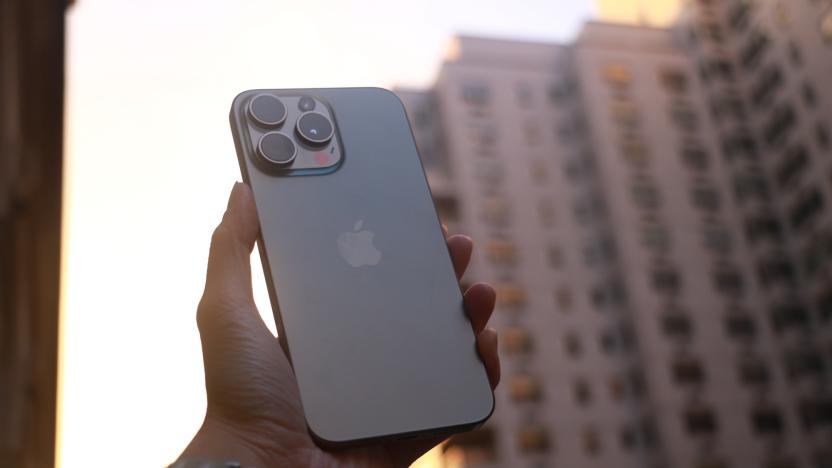 The iPhone 15 Pro Max held up in mid-air with a New York building in the background while the sun sets.