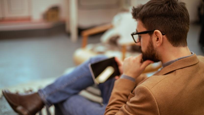 A rear view of a man sitting in a comfortable chair. He took his mobile phone to check the email.