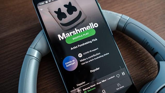 A phone displaying the Spotify app resting on a pair of headphones.