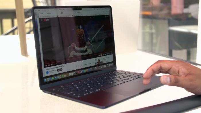 Review still of the M3 MacBook Air laptop sitting on a desk with a hand reaching towards its keyboard.