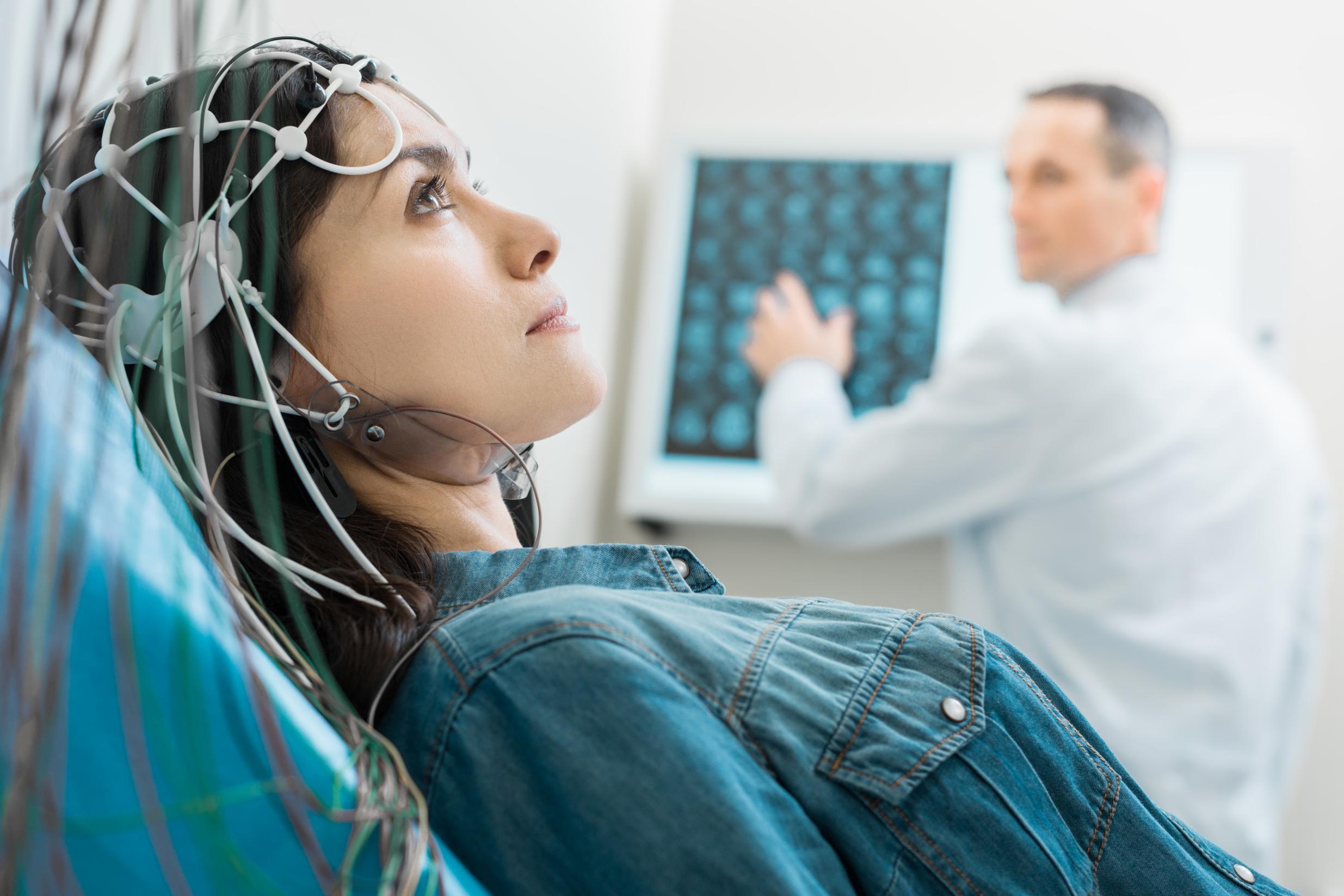 Vital procedure. Beautiful dark-haired woman lying on an examination table and undergoing electroencephalography while her doctor examining CT results