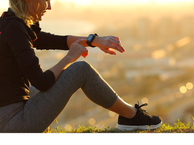 Runner sitting on the ground checking smartwatch after running at sunset