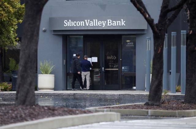 A man puts a sign on the door of the Silicon Valley Bank as an onlooker watches at the bank’s headquarters in Santa Clara, California, U.S. March 10, 2023. REUTERS/Nathan Frandino