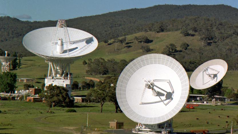 Several of the NASA Deep Space Network (DSN) satellite dishes on a grassy hillside with trees in the background.
