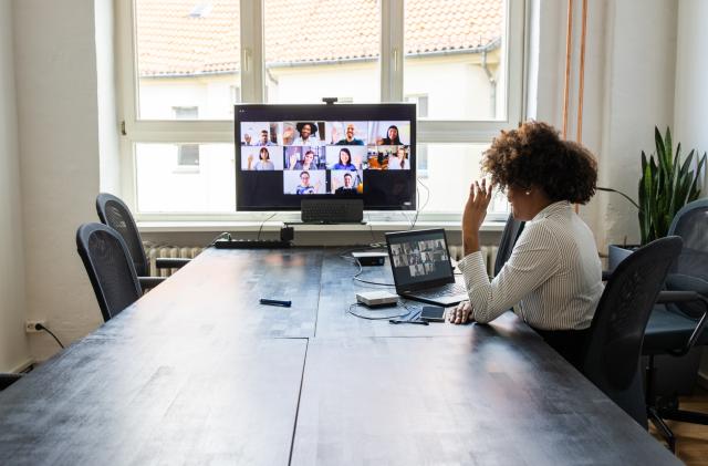 Rear view of a businesswoman having a meeting with team over a video conference in office board room. Meeting over a video call in office post pandemic lockdown.