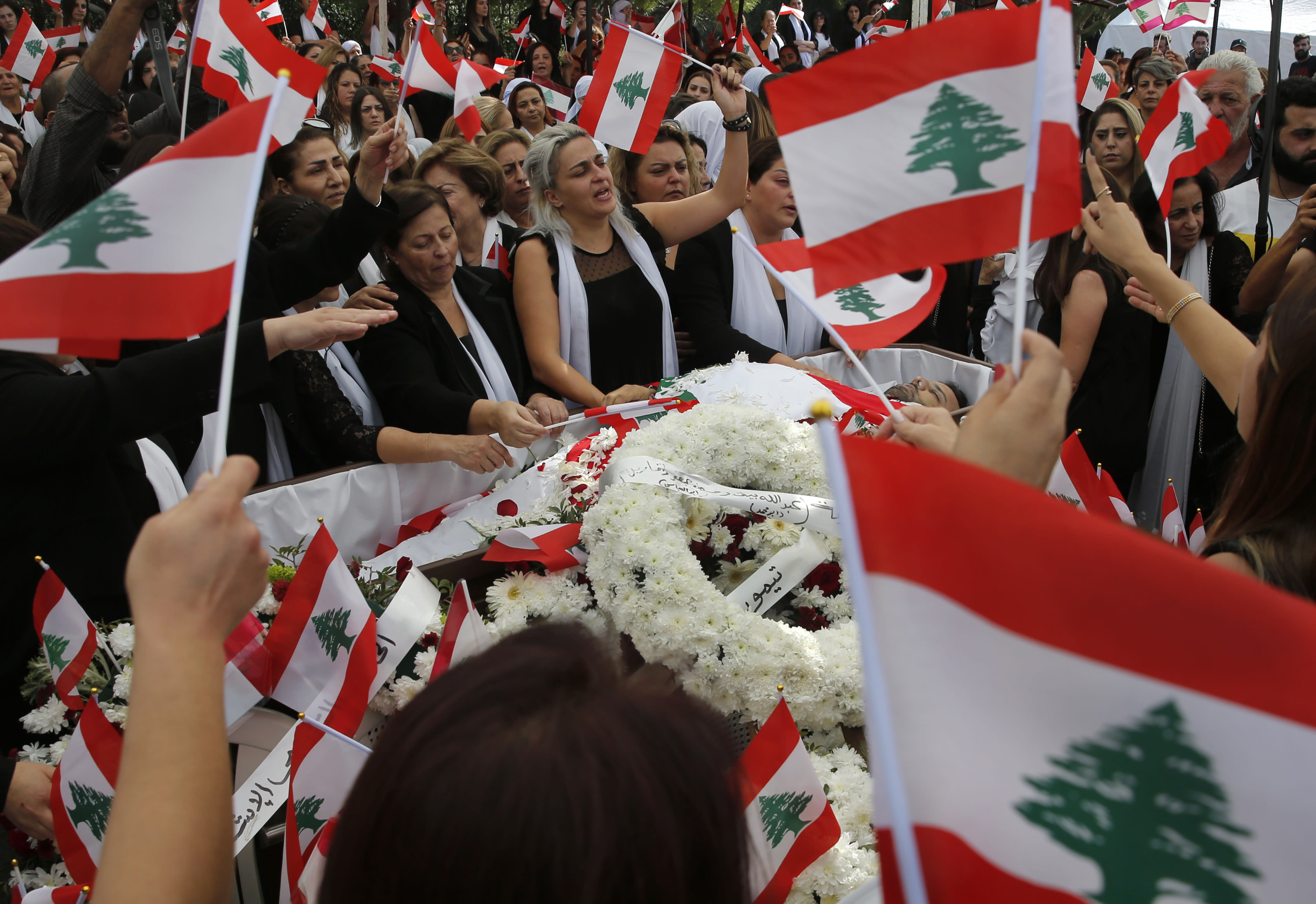 Lara, center, the wife of Alaa Abou Fakher, a man killed by a Lebanese soldier on Tuesday night protests in southern of Beirut, mourns with other relatives as they wave Lebanese flags over his body, during his funeral in Choueifat neighborhood, Lebanon, Thursday, Nov. 14, 2019. For nearly a month, the popular protests engulfing Lebanon have been startlingly peaceful. But the death of the 38-year-old father by a soldier, the first such fatality in the unrest, points to the dangerous, dark turn the country could be heading into. (AP Photo/Hussein Malla)