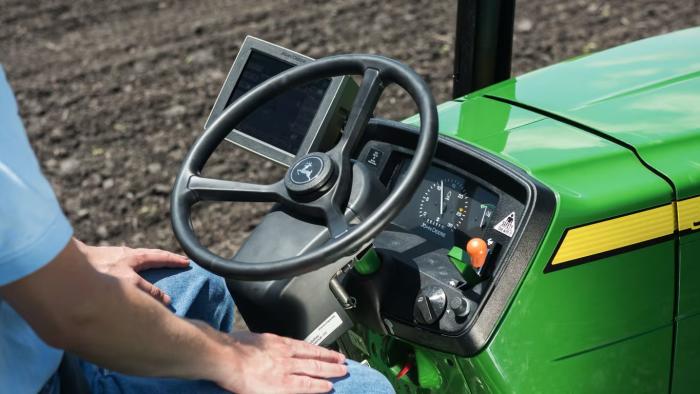 A John Deere tractor steering wheel pictured with a smart display next to it