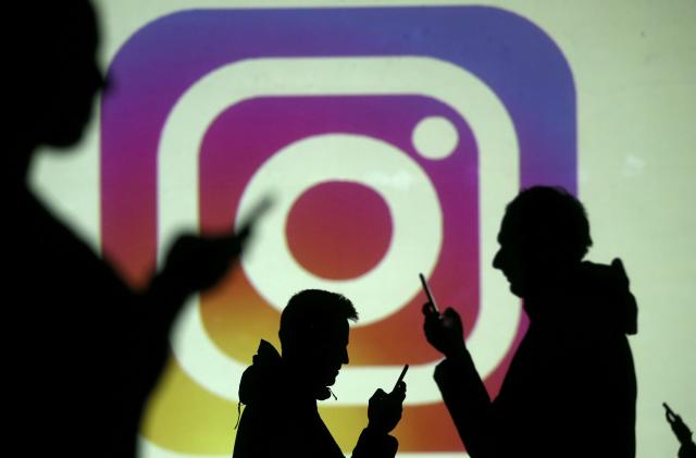 Silhouettes of mobile users are seen next to a screen projection of Instagram logo in this picture illustration taken March 28, 2018.  REUTERS/Dado Ruvic/Illustration