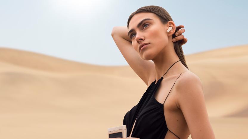 A model wearing an Urbanista Phoenix earbud and holding the charging case.