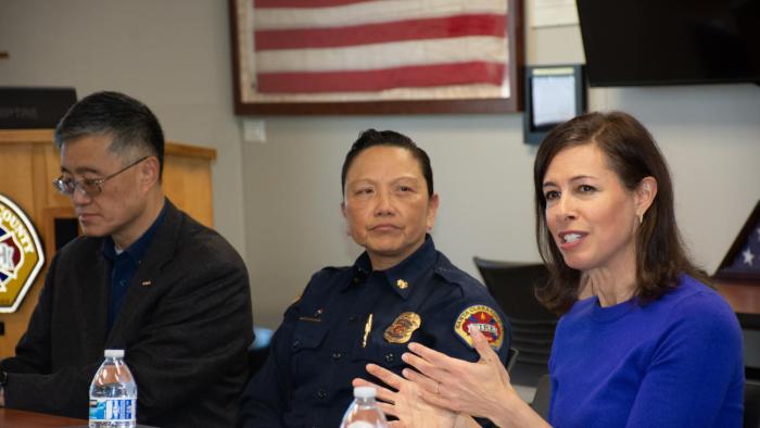 A man in black, a cop and a woman wearing a blue top sitting together.