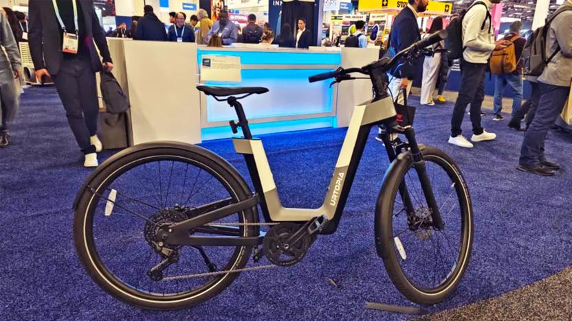 A grey, white and black Urtopia Fusion e-bike rests on its kickstand on the blue-carpeted CES 2024 showfloor.