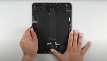 The new iPad Pro with the screen removed, a person's hands are seen holding it and using a tool to access pull tabs beneath one of the battery cells