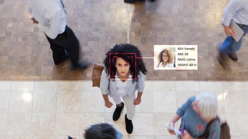 A young Hispanic businesswoman looks up while in an office lobby with businesspeople all around her. A facial recognition scan reveal her personal data.