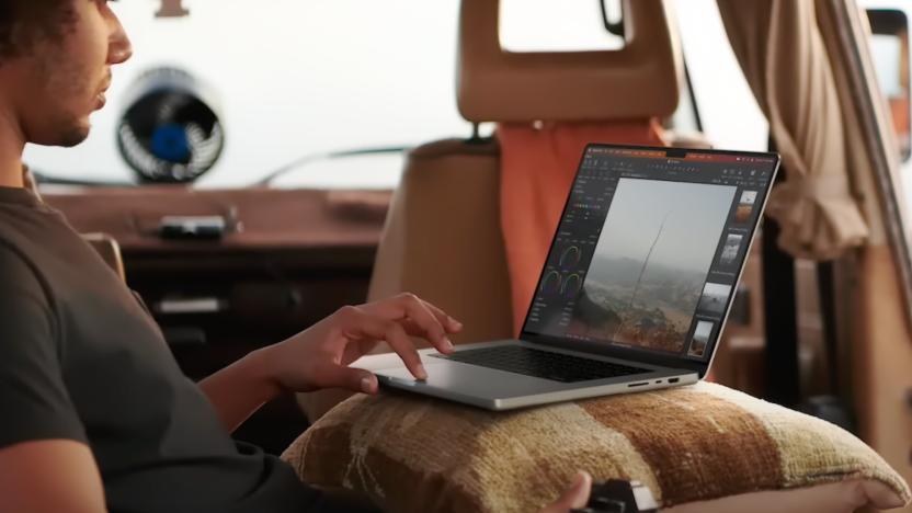 A man in a backseat of a van, working on a project on a new MacBook Pro