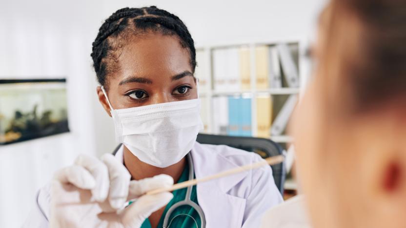 Serious young Black general practitioner in medical mask asking patient to open mouth so she could check her throat