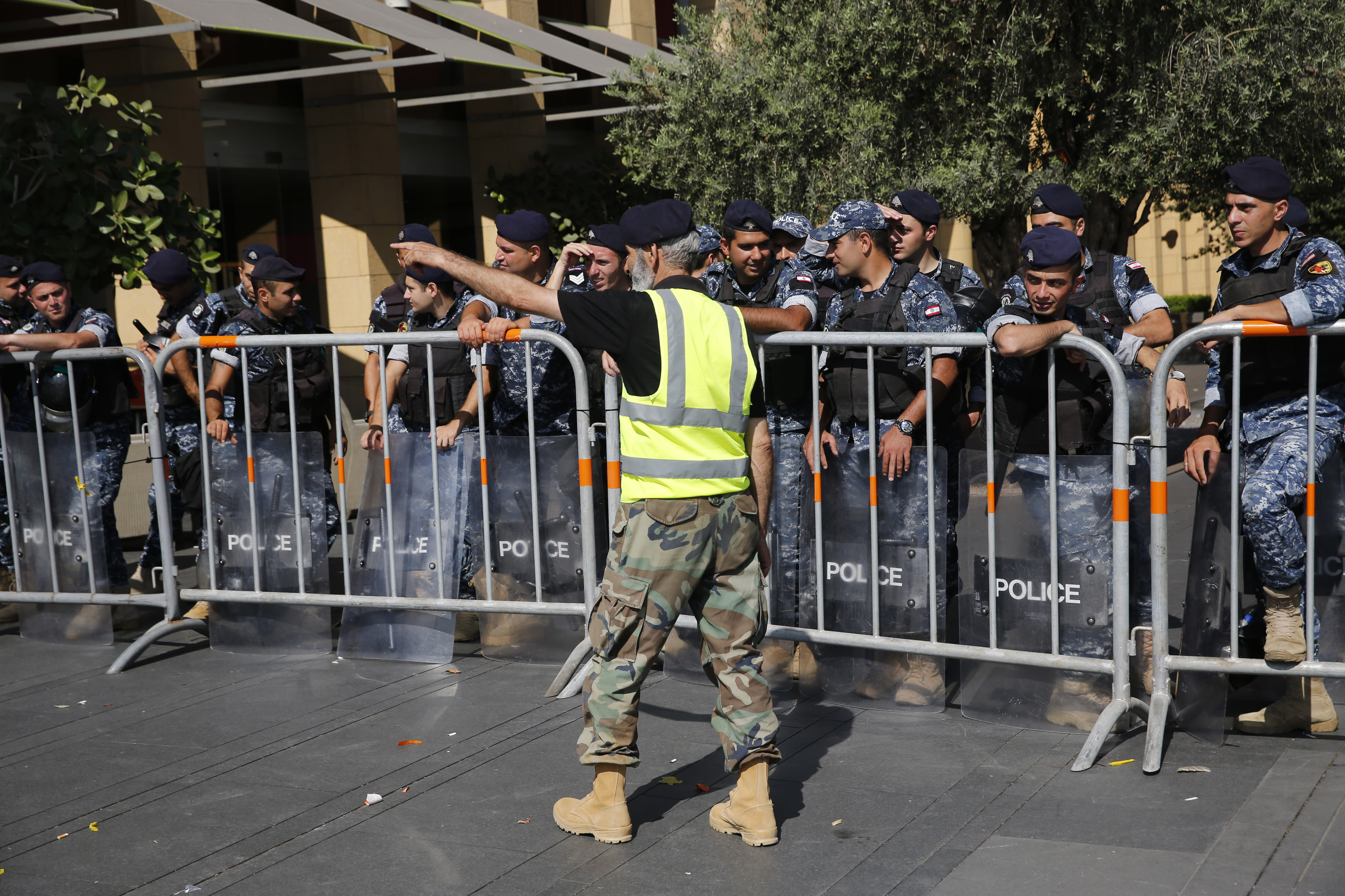 A retired Lebanese retired soldier, in yellow vest, protests in front of riot police who blocked a road leading to the parliament building where lawmakers and ministers are discussing the draft 2019 state budget, in Beirut, Lebanon, Tuesday, July 16, 2019. The lawmakers have begun discussing the budget amid tight security and limited protests against proposed austerity measures. The proposed budget aims to avert a financial crisis by raising taxes and cutting public spending in an effort to reduce a ballooning deficit. (AP Photo/Hussein Malla)