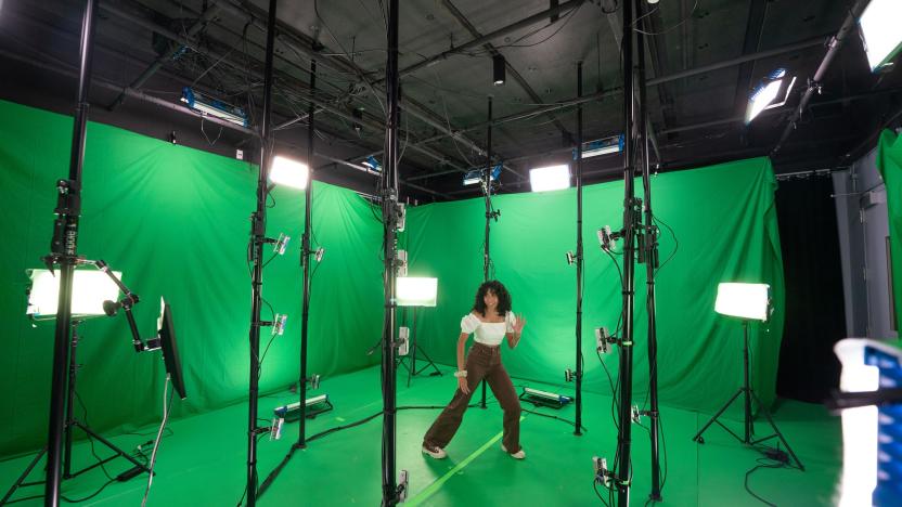 A dancer performs in a volumetric capture stage. Walls are draped with green screens as lights and sensors surround them.