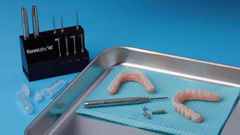 Image of some Formlabs Tools on a blue table, next to which is a steel medical tray with some 3D-printed implant dentures on a teal cloth and a silver screwdriver.