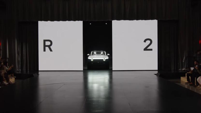 The Rivian R2 emerging from two withdrawing white panels on a stage at a launch event.