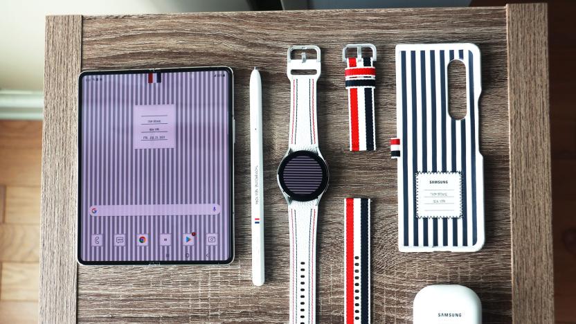 The Galaxy Z Fold 3, S Pen Pro, Galaxy Watch 4 and Buds 2 in Thom Browne editions laid out on a wooden surface.