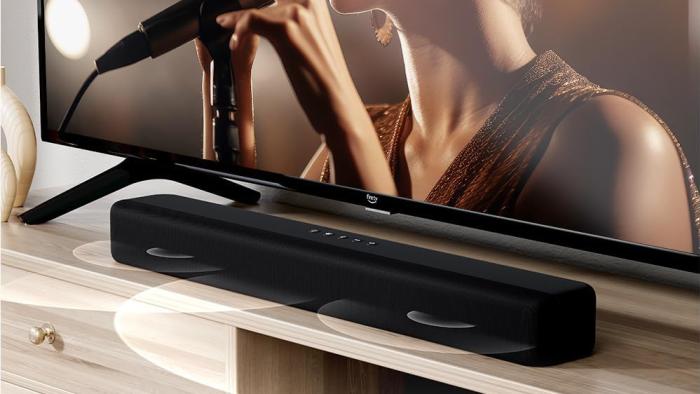 A soundbar on top of a console with a TV in the background.