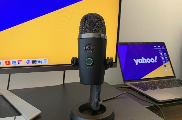 The Blue Yeti Nano microphone on a black desk riser in front of a laptop and a computer monitor.