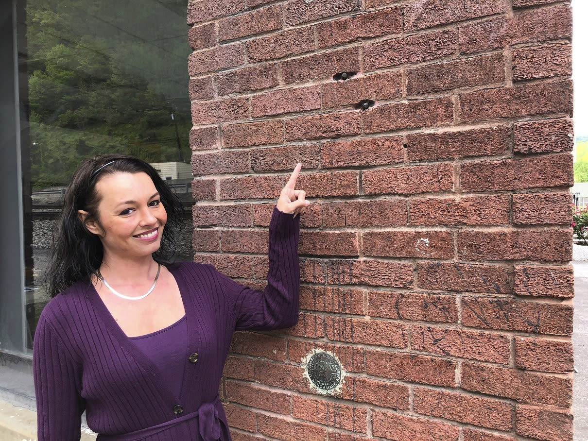 In this Tuesday, May 12, 2020, photo, West Virginia Mine Wars Museum tour guide Kim McCoy points to bullet holes still visible from a gunfight between miners and detectives hired by a coal company in Matewan, W.Va. Ten people died in the Matewan Massacre on May 19, 1920. McCoy is a great niece of Sid Hatfield, the Matewan police chief who sided with the miners and was involved in the shootings. Hatfield was shot to death a year later by coal company detectives. (AP Photo/John Raby)