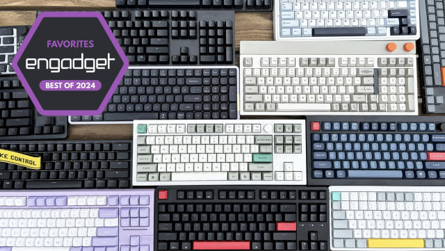 A wide selection of mechanical keyboards in different sizes, shapes and colors sit in close proximity to one another on top of a brown wooden table.